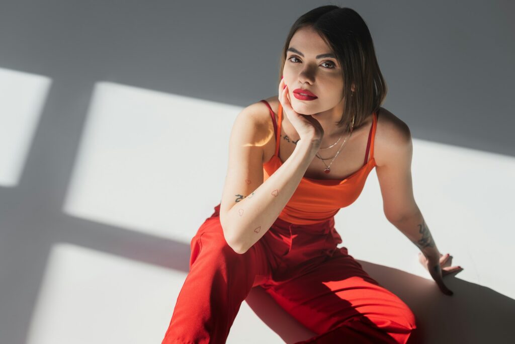 high angle view of young tattooed woman with short hair sitting in suit on grey background,